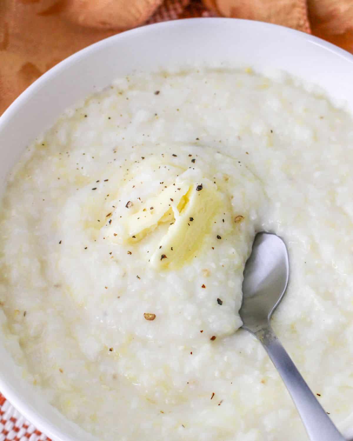 A white bowl filled with slow cooker grits, butter, salt, and black pepper.