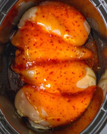 A slow cooker with chicken and sweet chili sauce on the chicken.
