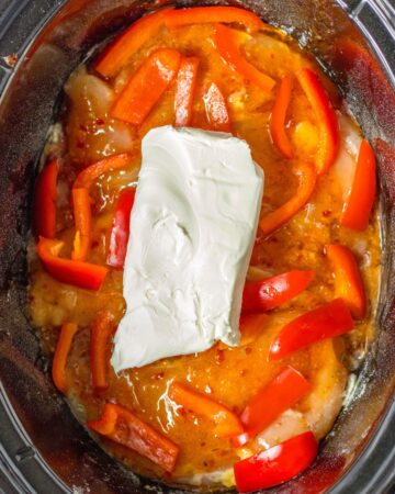 Raw chicken topped with chicken, peppers, and cream cheese to make sweet chili chicken. 