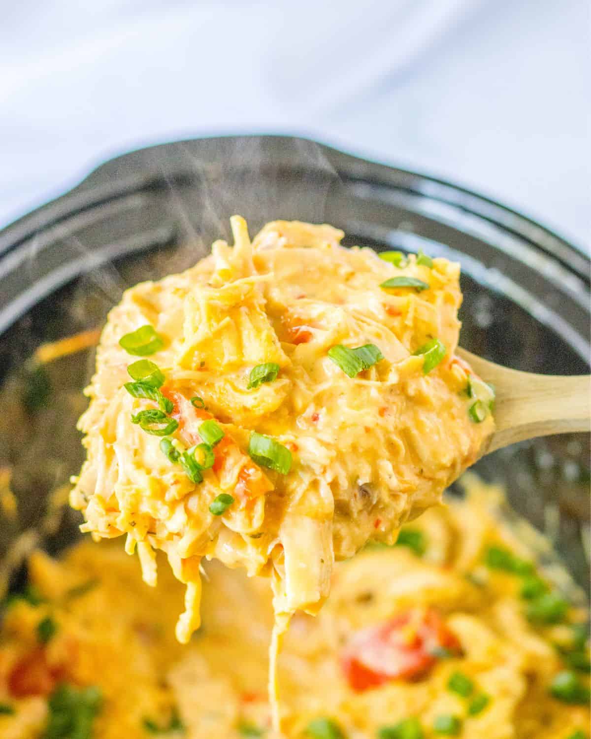 Slow cooker chicken in a chili sauce being picked up with a wooden spoon. 