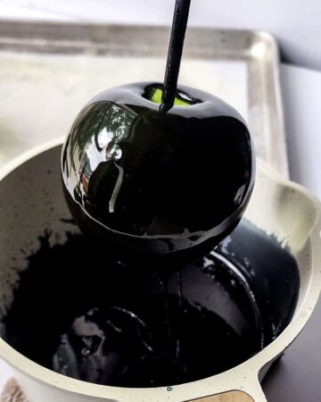 A black candy coating with an apple being dipped into the bowl. 