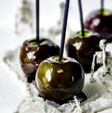 Poison candy apples on a plate with a silver skeleton behind it.