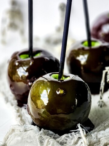 Poison candy apples on a plate with a silver skeleton behind it.