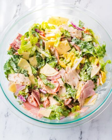 A glass bowl of Italian sub dip made with Italian cold cuts, lettuce, banana peppers in a creamy sauce.