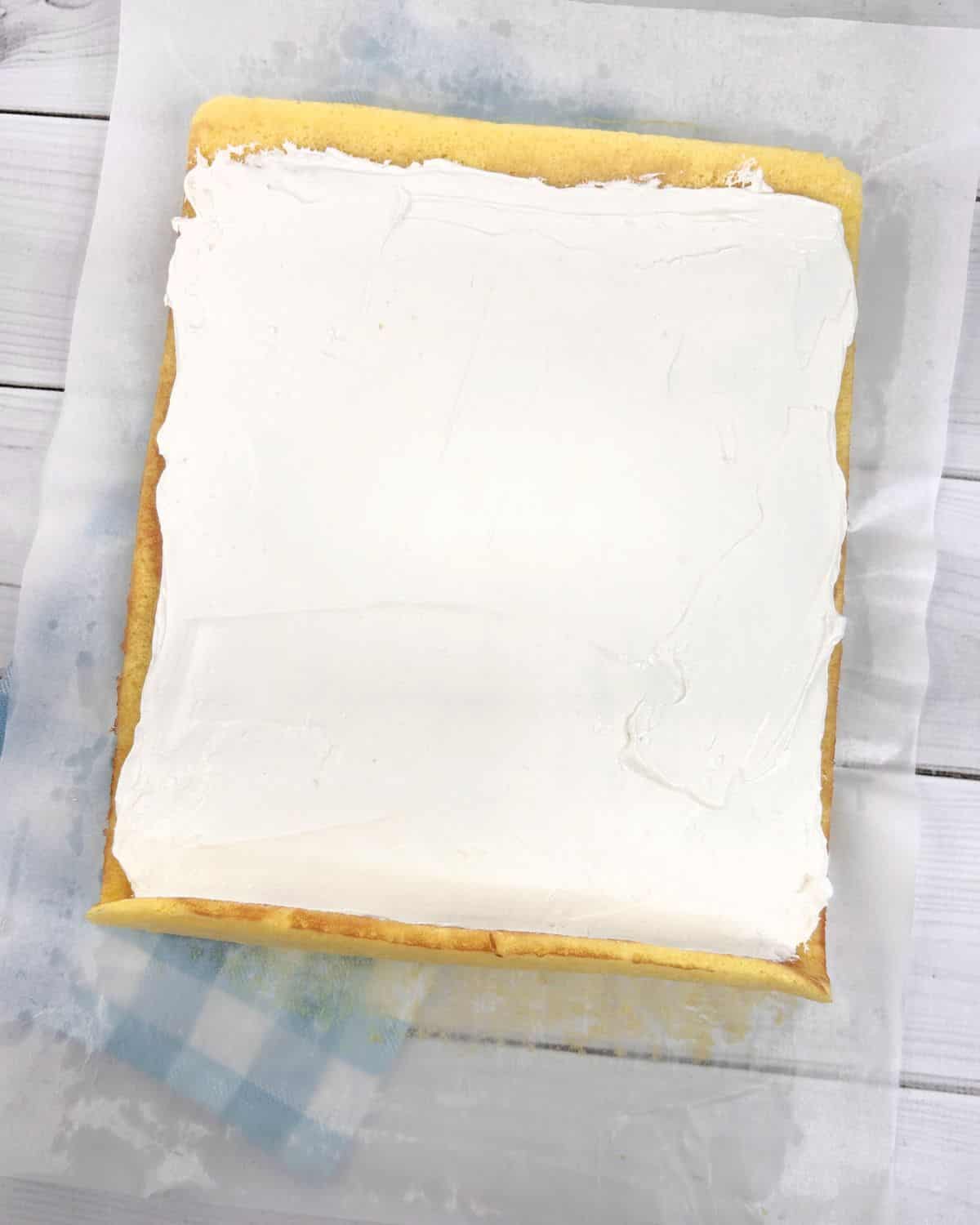 A lemon sponge cake with whipped cream topping being ready to roll.