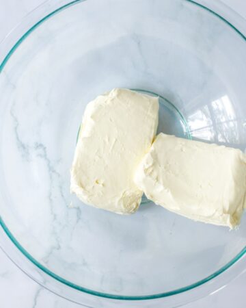 A glass bowl with two blocks of cream cheese in the bowl. 