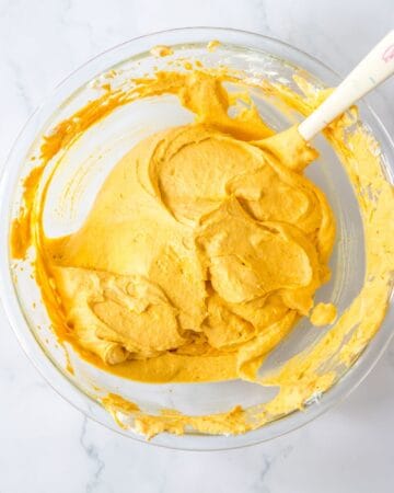 A glass bowl of pumpkin puree and cream cheese whipped together. 