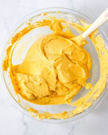 A glass bowl of pumpkin puree and cream cheese whipped together. 