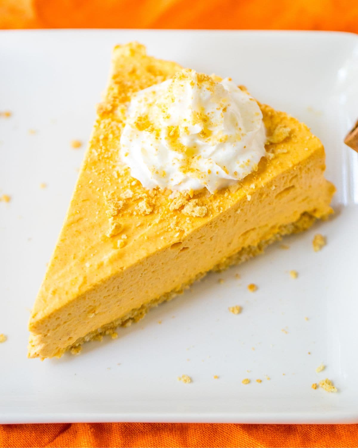 A slice of no bake pumpkin cheesecake with a graham cracker crust topped with whipped cream and crumbled pumpkin. 