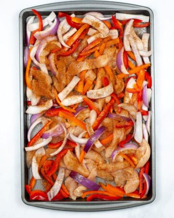 A sheet pan of chicken peppers and onions with fajita seasoning.