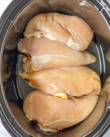 Slow cooker with boneless chicken breasts in the vessel. 