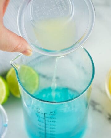 Blue Curacao liquor in a glass with lime juice being poured in to the glass as the first step to make Tipsy Mermaid. 