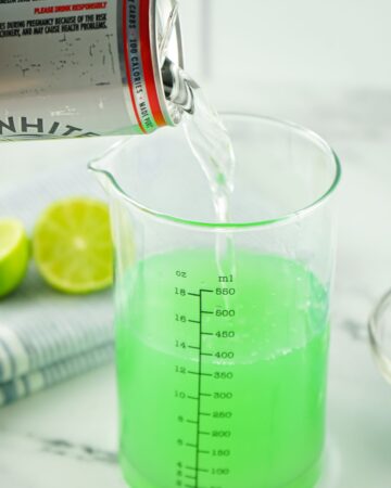 The second step to make a tipsy mermaid is pouring the hard seltzer into the glass with liquor. 