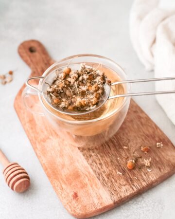 A glass bowl with a strainer in the glass filled with dried chamomile leaves to make iced latte.