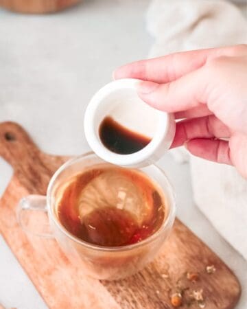 A glass cup with chamomile tea and vanilla extract being poured into the bowl to make iced chamomile latte