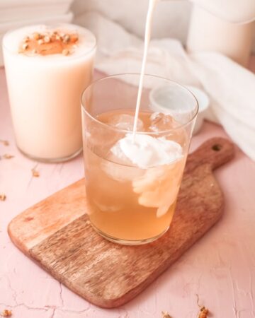 A glass half filled with chamomile tea and milk being poured into the glass.