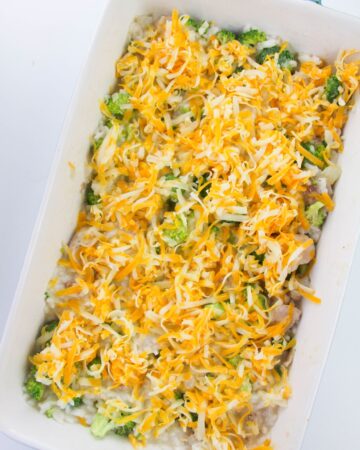 Broccoli, rice, chicken in a creamy casserole dish topped with shredded cheese.