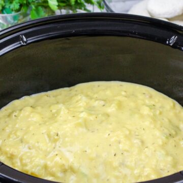 A slow cooker with chicken and vegetables topped with cream of chicken soup.
