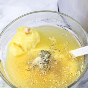 A glass bowl with cream of chicken soup, chicken broth, and spices to make the sauce for slow cooker chicken pot pie.