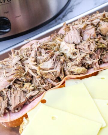 A loaf of Italian bread sliced open with swiss cheese on one side and ham and shredded pork on the other sliced loaf.