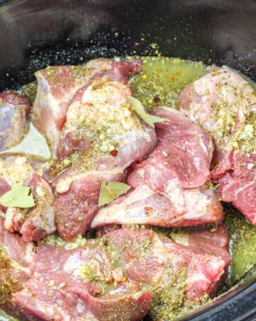 The vessel of a slow cooker with pork seasoned with spices and lime juice.