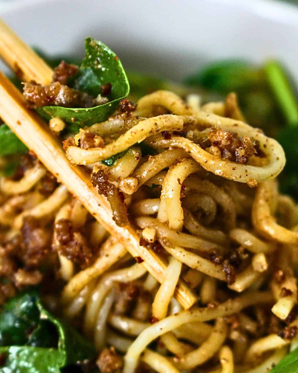 Noodles in Dandan sauce being picked up in chopsticks. 