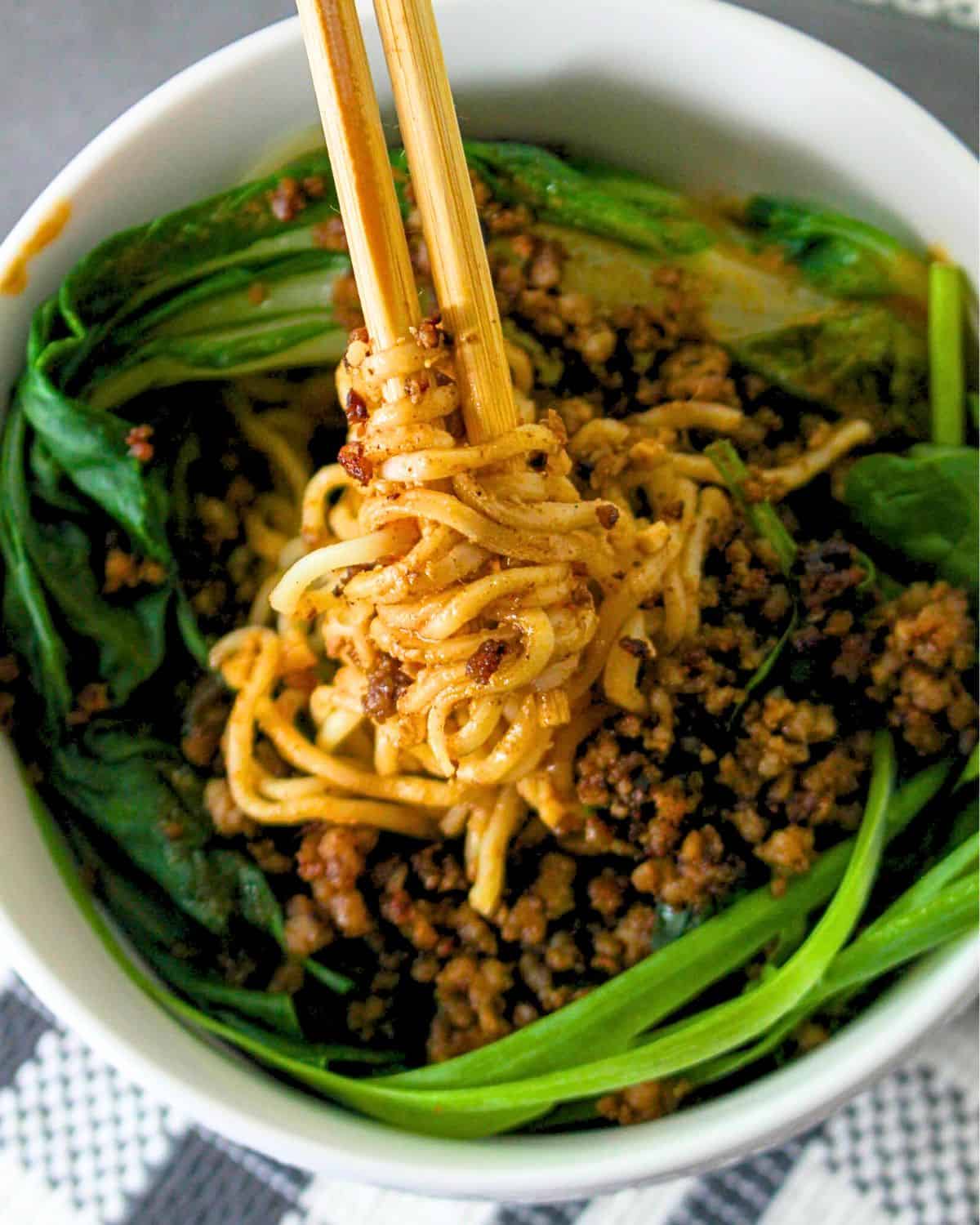 A bowl of bokchoy topped with chopped cooked pork and noodles in DanDan sauce. 