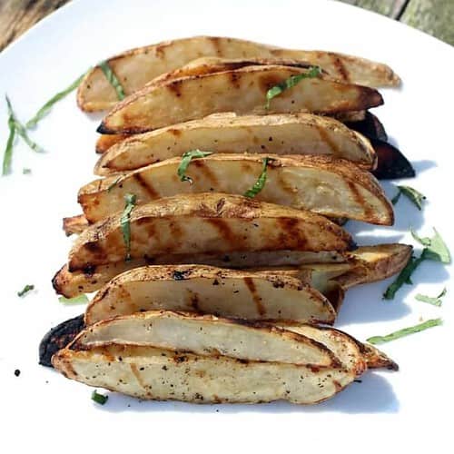 Grilled potato wedges on a plate sprinkles with chopped parsley.