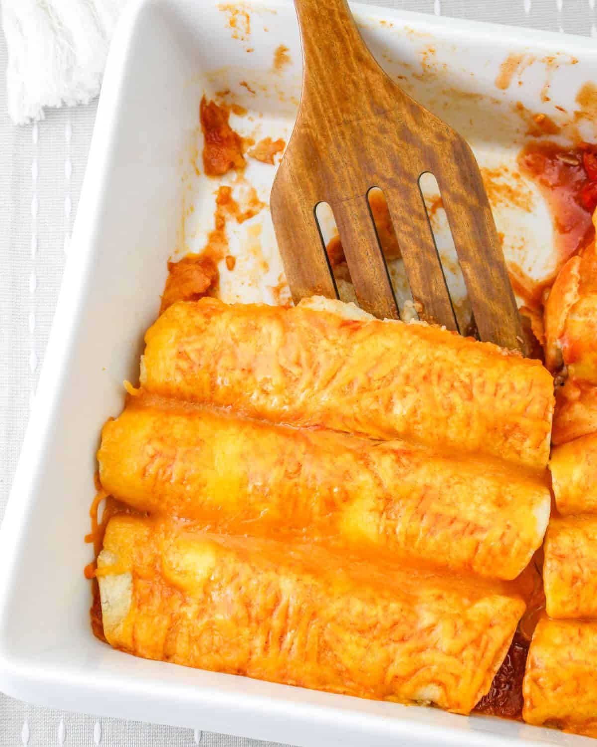 Shredded beef enchiladas topped with cheese and enchilada sauce being picked up out of the casserole.