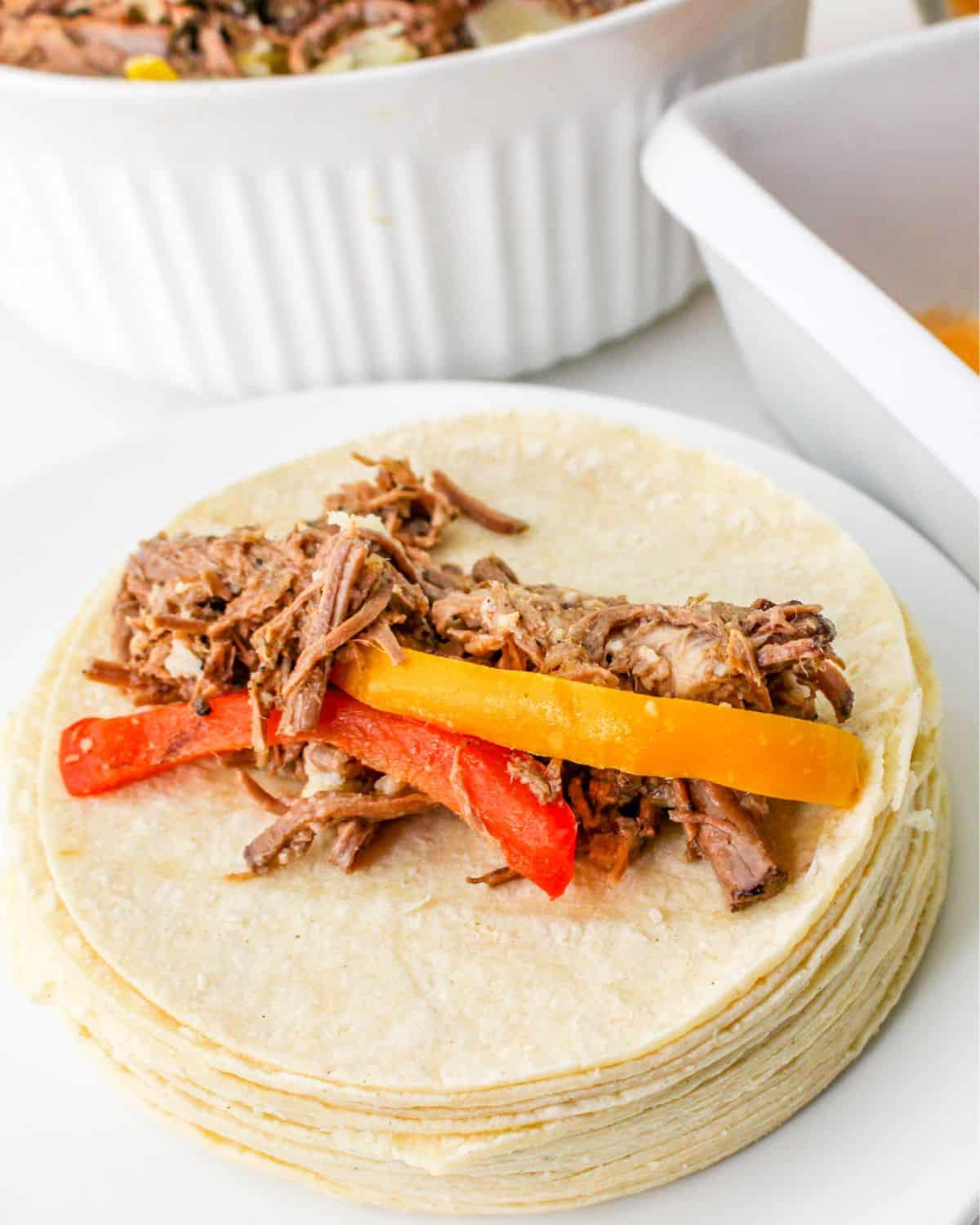 Corn tortillas with leftover shredded beef and peppers on top of the tortilla.