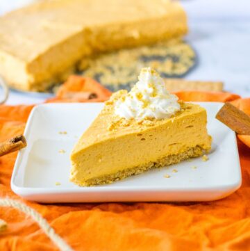 Pumpkin Pie cheesecake, a no bake dessert with whipped cream on top on a square dessert plate.