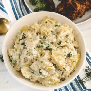 A bowl of potato salad with a creamy dressing and chopped dill on top.