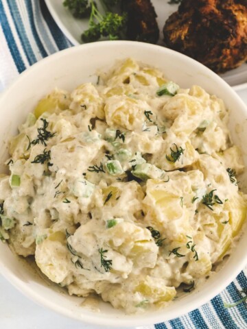 A bowl of potato salad with a creamy dressing and chopped dill on top.