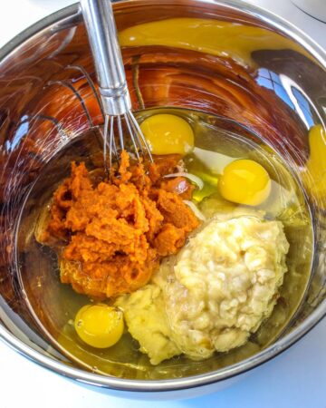 A large mixing bowl with pumpkin puree, banana, and spices to make a pumpkin banana chocolate bread. 