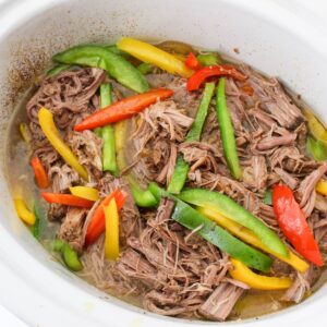 A slow cooker vessel with shredded beef and peppers.