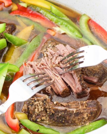 Beef being shredded in a slow cooker with peppers.