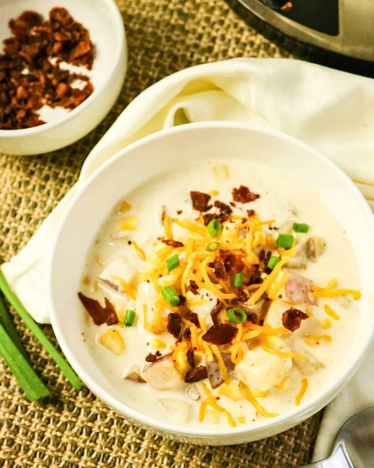 Slow cooker corn chowder in a bowl with potatoes, cheddar cheese, chopped bacon, and chives.