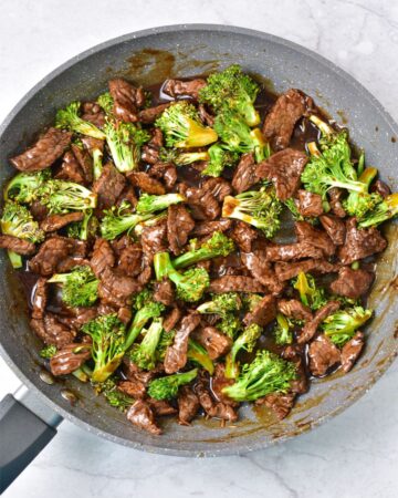 A large pan with beef and broccoli that has been stir fried. 