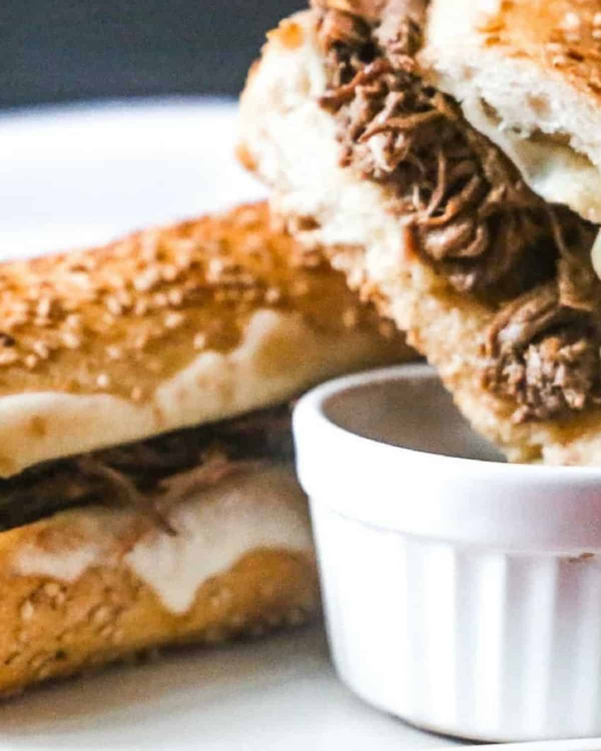 Slow cooker french dips being dipped into au jus sauce.