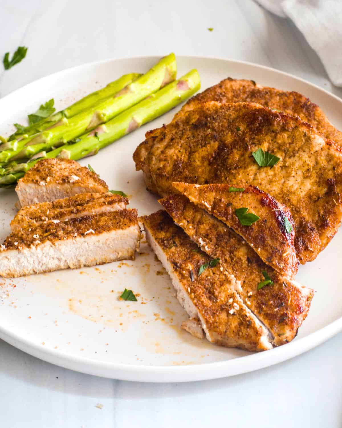 A white plate with pork chops made in the air fryer with asparagus.