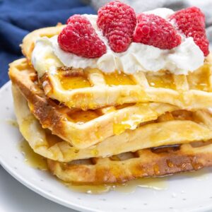 Easy buttermilk waffles topped with whipped cream and raspberries.