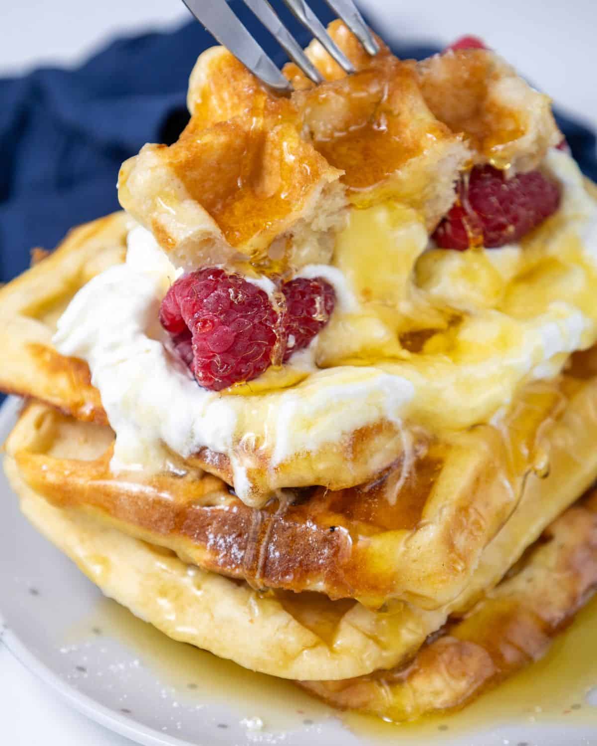 A stack of buttermilk waffles with whipped cream, syrup, and raspberries.