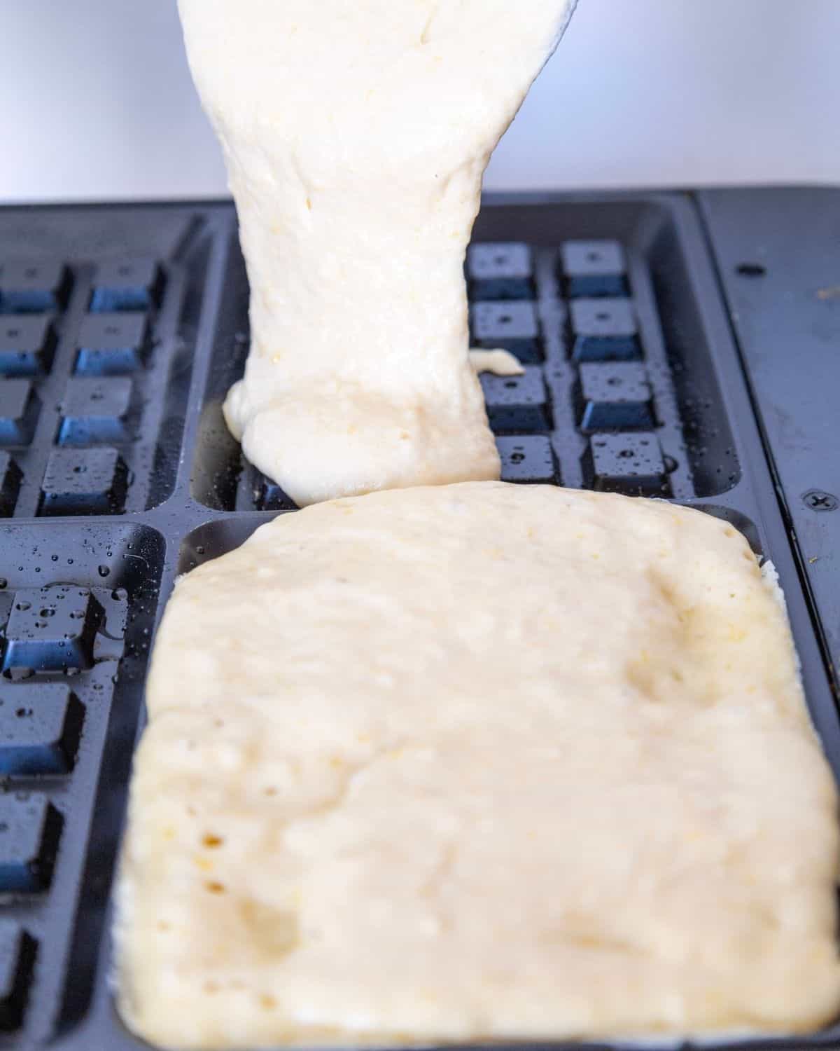 A waffle maker with the batter being poured in to make waffles.