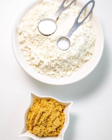 A bowl of flour with salt, baking soda, and baking powder with brown sugar in a side bowl.