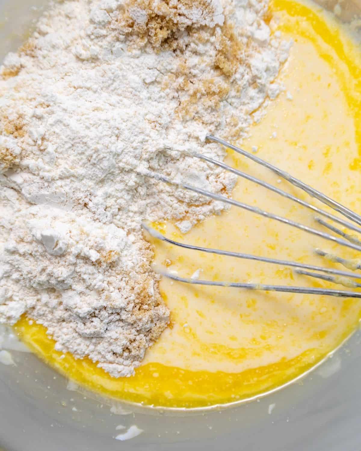 The wet ingredients with dry ingredients being added in to a glass bowl to make waffles.