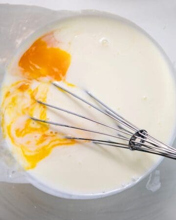 A bowl of waffle mixture with eggs being blended into the mixture.