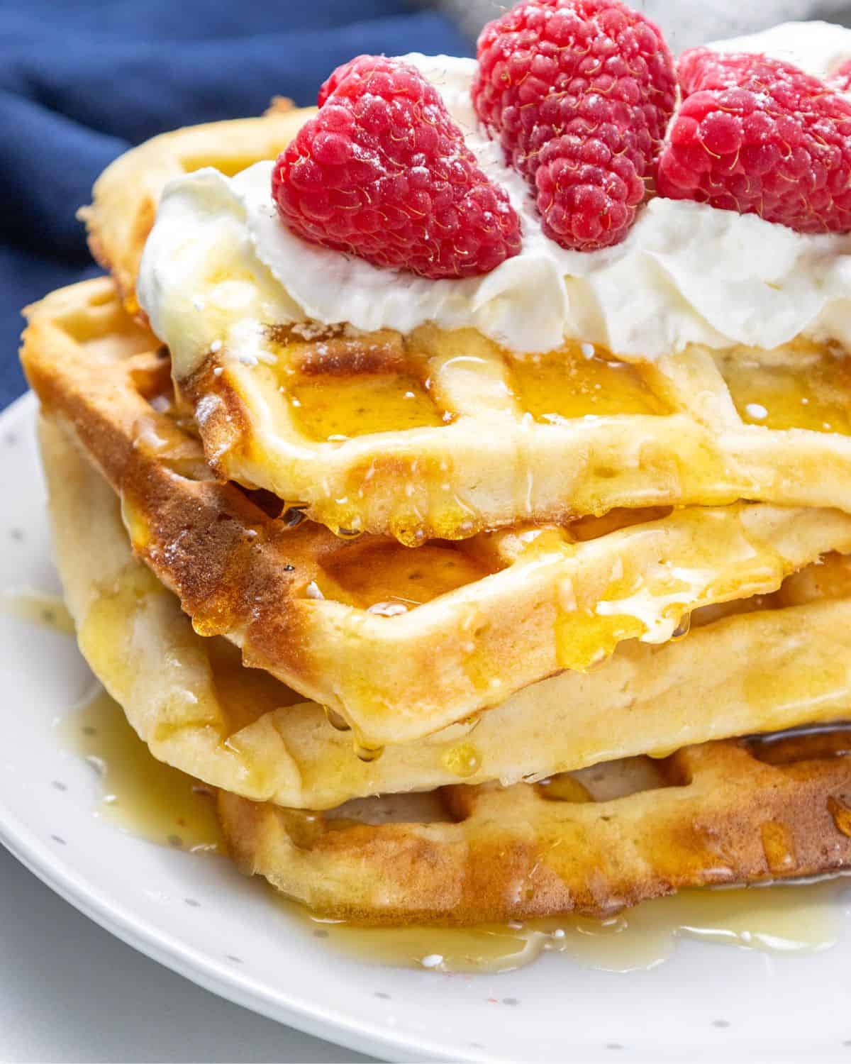 A stack of copycat eggo waffles topped with whipped cream. raspberries, and syrup.