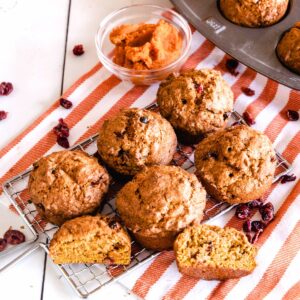 Pumpkin Muffins with dried cranberries on a baking rack with dried cranberries and a bowl of pumpkin puree on the side.