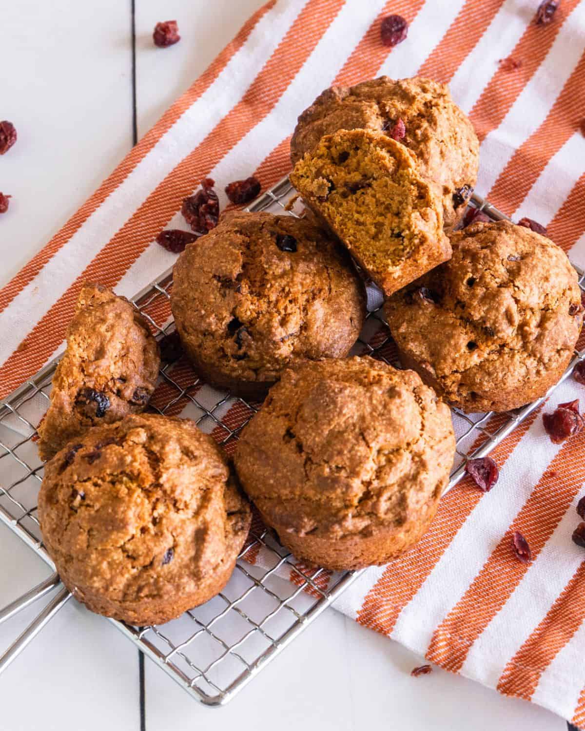 Cranberry pumpkin muffins are stacked on a striped linen napkin. 