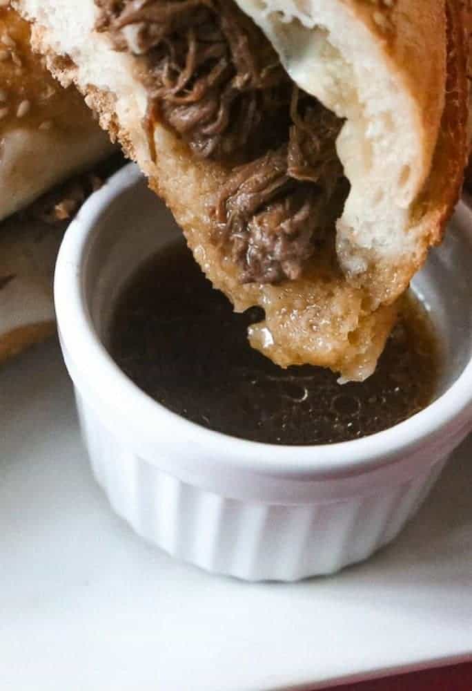 Slow Cooker French Dip Sandwich being dipped into an aus jus sauce. 